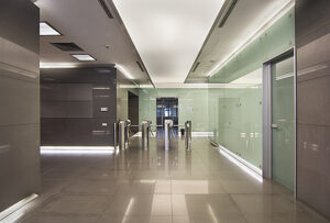 Commercial office lift hall with glass walls, polished stone flooring, recessed lighting, and modern elevator design.