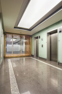 Commercial office lift hall with glass walls, polished stone flooring, recessed lighting, and modern elevator design.
